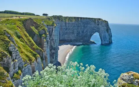 Falaises d'Étretat, France. L'arche naturelle de la Porte d'Aval se dresse fièrement au-dessus de la plage de galets. Le **gr 21** serpente le long de la côte verdoyante.