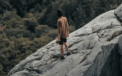 Un homme sur un rocher escarpé, le regard perdu dans le lointain, semble lutter contre sa peur du vide.