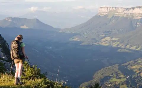 Randonneuse contemplant un panorama grandiose lors d'une traversée de la Chartreuse. Les montagnes s'étendent à perte de vue.