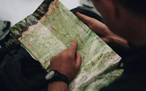 Un randonneur consulte une carte IGN des plateaux du Vercors, pointant un chemin sur le terrain.