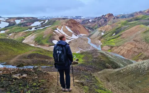 Un randonneur admire le paysage coloré de Landmannalaugar, avec ses montagnes aux teintes ocre, vertes et blanches.