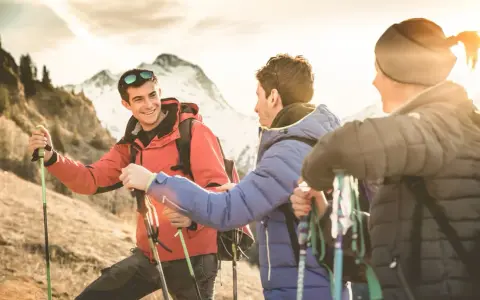 Trois randonneurs souriants, prêts pour une reconversion accompagnateur moyenne montagne, profitent du soleil couchant sur les sentiers.