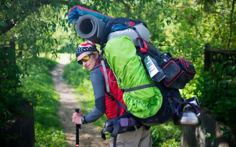 Un randonneur, prêt pour l'aventure, montre comment porter un sac à dos bien chargé avec une couverture de sol et une bouilloire.