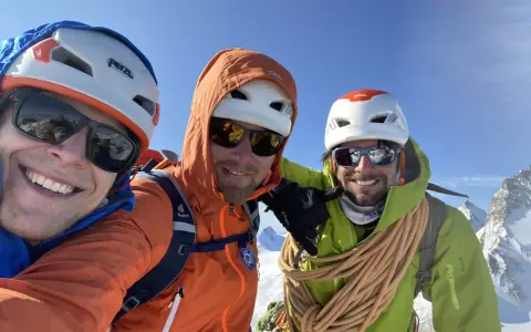 Trois alpinistes souriants au sommet, prêts à devenir guide de haute montagne à 40 ans. Corde et équipement de sécurité visibles.