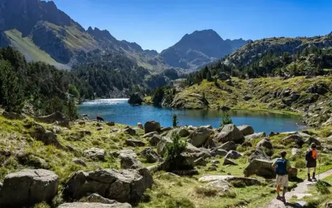 Deux randonneurs explorent un sentier rocailleux menant à un lac bleu étincelant, entouré de montagnes majestueuses. Une parfaite randonnée Val d'Aran.