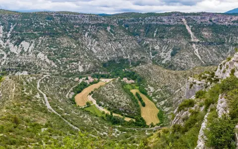 Vue aérienne du cirque de Navacelles, un méandre de rivière creusé dans un paysage de garrigue et de falaises calcaires, avec un village niché au fond.