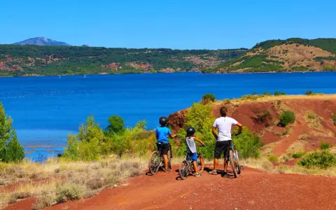 Famille à vélo profitant d'une randonnée au lac du Salagou, avec ses eaux bleues et ses collines rouges.