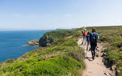 Randonneurs sur le sentier côtier GR34, profitant de la vue sur la mer et les falaises. La distance semble longue, mais le paysage est magnifique.