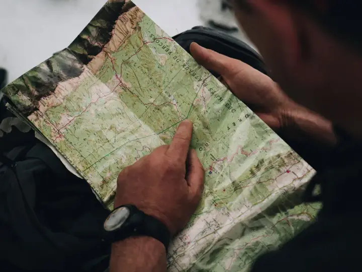 Un randonneur consulte une carte IGN des plateaux du Vercors, pointant un chemin sur le terrain.