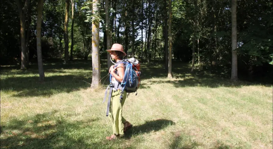 Une randonneuse avec un sac à dos et une poche à eau visible. Elle est dans une forêt, prête pour son aventure.
