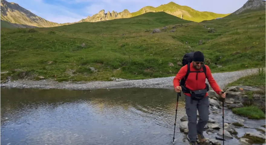 Un randonneur traverse un ruisseau de montagne, bâtons en main. Une belle illustration de pourquoi marcher avec des bâtons pour plus de stabilité.