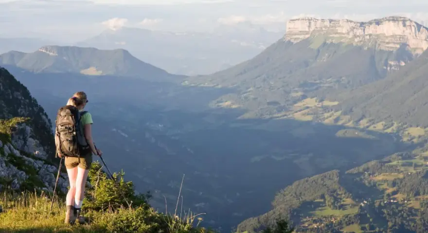 Randonneuse contemplant un panorama grandiose lors d'une traversée de la Chartreuse. Les montagnes s'étendent à perte de vue.