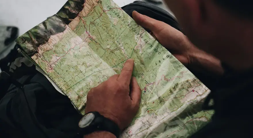Un randonneur consulte une carte IGN des plateaux du Vercors, pointant un chemin sur le terrain.