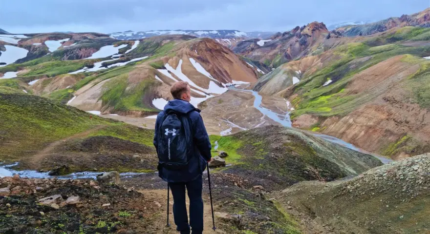 Un randonneur admire le paysage coloré de Landmannalaugar, avec ses montagnes aux teintes ocre, vertes et blanches.