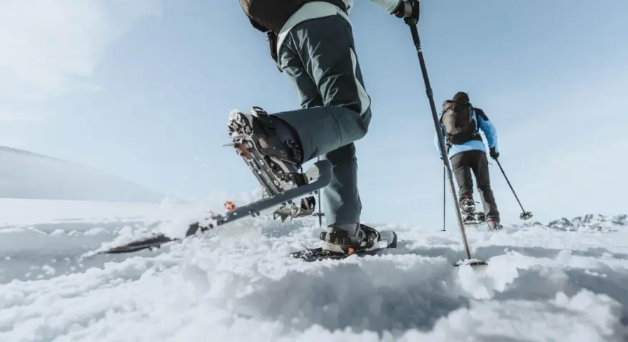 Deux personnes font une randonnée hivernale en raquettes sur un paysage enneigé sous un ciel bleu clair.