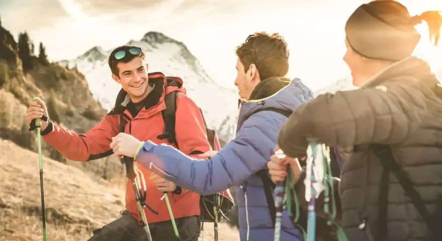 Trois randonneurs souriants, prêts pour une reconversion accompagnateur moyenne montagne, profitent du soleil couchant sur les sentiers.