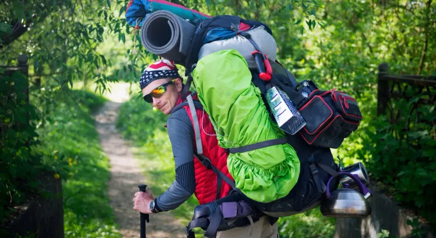 Un randonneur, prêt pour l'aventure, montre comment porter un sac à dos bien chargé avec une couverture de sol et une bouilloire.