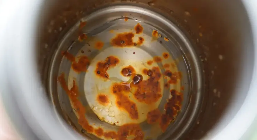 Intoxication eau gourde : intérieur rouillé d'une gourde, avec des dépôts orangés et de l'eau trouble.