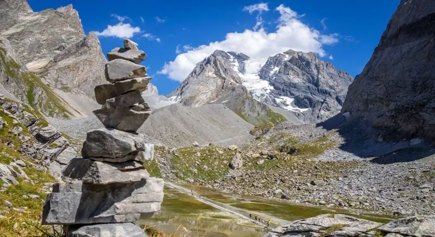 Un cairn, une pile de pierres, marque le chemin dans un paysage de montagne spectaculaire, avec un glacier au loin.