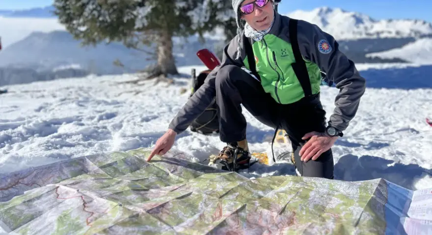 Un homme en tenue de ski pointe une carte sur la neige, planifiant son ascension vers le plus haut sommet de France.