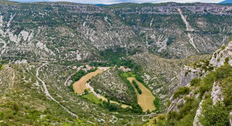 Vue aérienne du cirque de Navacelles, un méandre de rivière creusé dans un paysage de garrigue et de falaises calcaires, avec un village niché au fond.