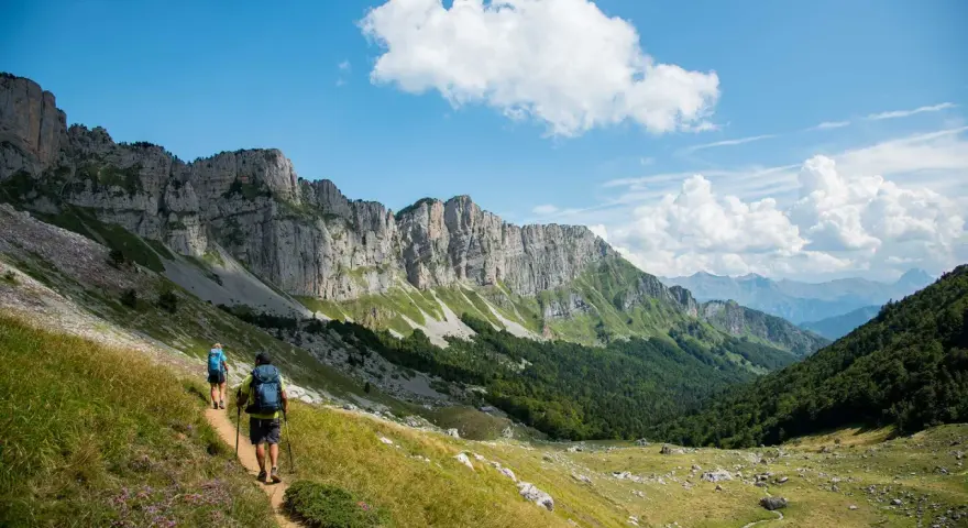 Deux randonneurs explorent un sentier escarpé au Pays Basque, sous un ciel bleu et des falaises imposantes.