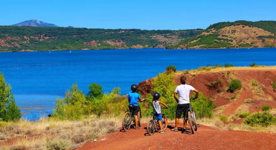 Famille à vélo profitant d'une randonnée au lac du Salagou, avec ses eaux bleues et ses collines rouges.