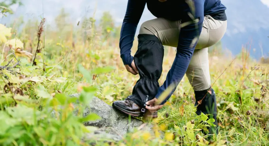 Une personne ajuste ses guetres de randonnée dans un paysage naturel.
