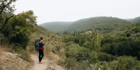 Randonneuse avec sac à dos sur un chemin d'amadou, contemplant une vallée verdoyante. La carte du chemin d'amadou est dans sa poche.